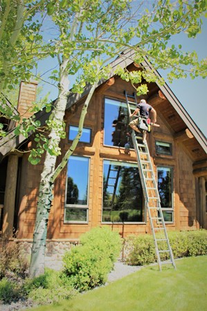 Member of Purity Cleaning and Restoration Services cleaning large windows on outside of home.